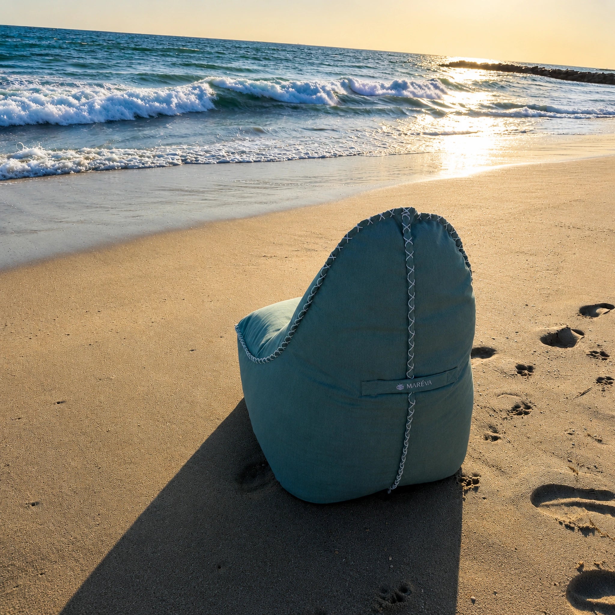 MARÉVA Lounger + Footrest in Coastal Sage on a sandy beach with ocean waves in the background