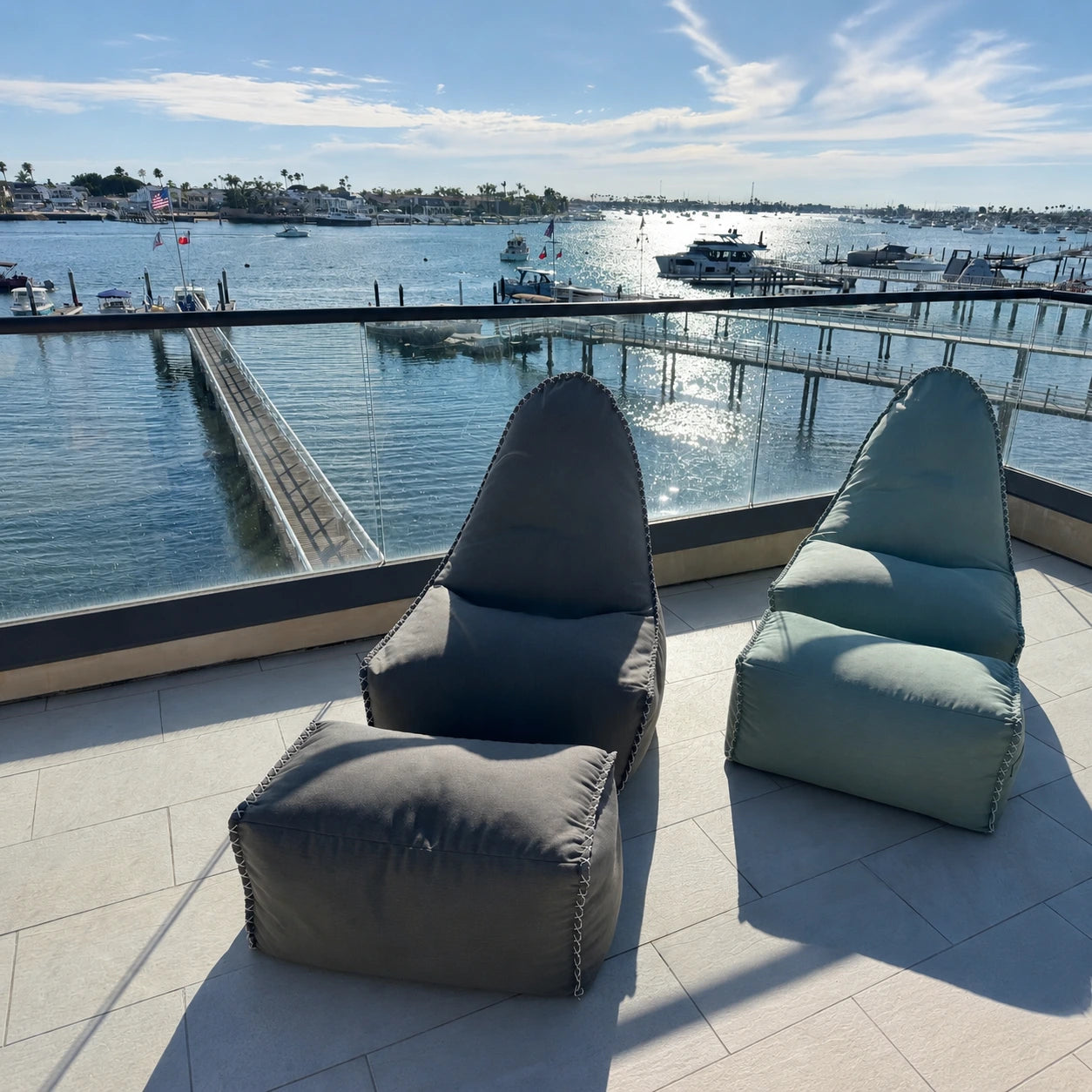 Two MAREVA Loungers and footrests on a patio, shown in Coastal Sage, with a marina view.